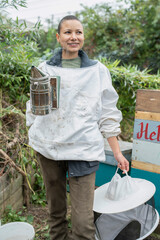 Wall Mural - Portrait of smiling female beekeeper holding smoker in urban garden