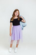cheerful preteen girl in black t-shirt, violet skirt and white sneakers posing and standing on white background