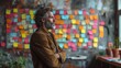 Man contemplating ideas, colorful sticky notes on wall.