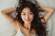 © Patcharaphon - Portrait of smiling Asian beautiful woman lying down on her bed at home in the morning