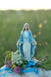 Madonna figurine and flowers outdoor, abstract natural background. Blessed praying Mother of God, Grace Virgin Mary statue. Herbal consecration - customs on Assumption of Mary day. religion ritual