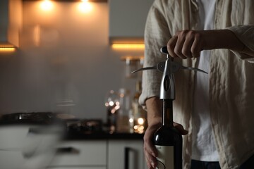 Wall Mural - Man opening wine bottle with corkscrew in kitchen, closeup. Space for text