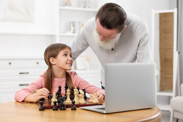 Wall Mural - Grandfather teaching his granddaughter to play chess following online lesson at home