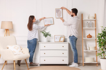 Wall Mural - Man and woman hanging picture frames on white wall at home
