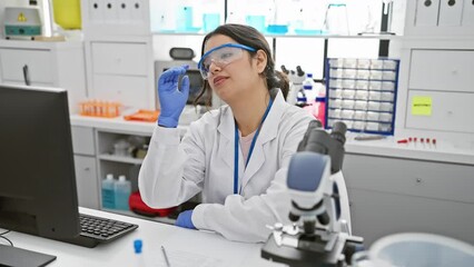 Canvas Print - Tired, bored, and depressed, a young, beautiful hispanic woman scientist, in safety glasses, struggles with problems at the lab, arms crossed