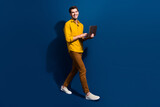 Fototapeta Panele - Full body photo of attractive young guy walking hold netbook smm manager wear trendy yellow clothes isolated on dark blue color background