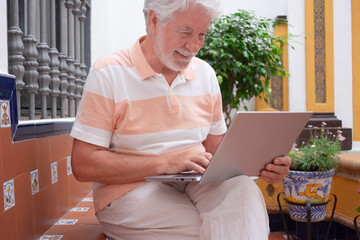 Sticker - Relaxed senior bearded man  using laptop sitting outdoors in the patio browsing shopping typing. Wireless technology