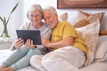 Wall Mural - Video call concept. Portrait of happy senior couple communicating in remote chat with family and friends - Grandparents with digital tablet sitting in bed, wireless technology