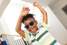African American Boy Dances Joyfully, Wearing Blue Sunglasses And A Striped Shirt
