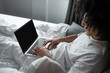 © zinkevych - Brunette man in white tshirt lying in bed and working on laptop
