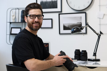 Canvas Print - Professional photographer in glasses holding digital camera at table in office