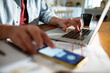 © Marko Geber - Close-up of a man's hands using laptop and smartphone at home office desk