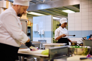 Wall Mural - Young black female cook preparing meal while working in restaurant.