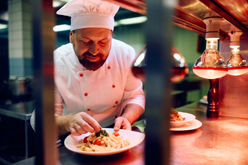 Wall Mural - Professional chef serving pasta while preparing food in  kitchen.