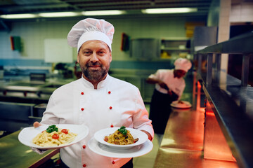 Wall Mural - Smiling professional chef serving dish in restaurant and looking at camera.