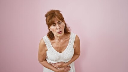 Sticker - Middle age woman wearing dress standing in pain over isolated pink background, hand on stomach suffering from painful ache, nauseous expression revealing disease.