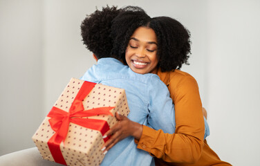 Wall Mural - Radiant African American woman with a bright smile hugs a man while holding a gift