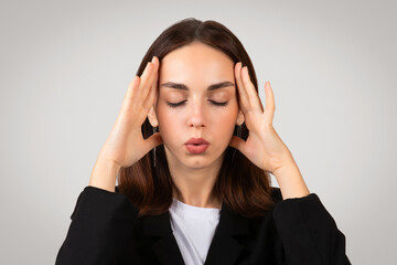 Focused businesswoman in a tailored black suit with closed eyes holds her temples