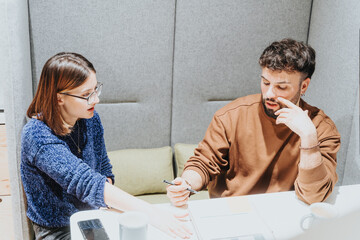 Poster - Two young professionals engaged in a serious discussion over documents at a workplace, showcasing teamwork and problem-solving in a corporate environment.