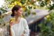 Woman enjoying a refreshing glass of homemade kombucha while basking in the sunlight The image showcases her healthy lifestyle and love for natural remedies With a backdrop of lush greenery, she
