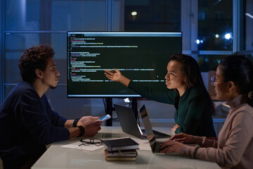 Group of three young ethnically diverse programmers working together on code in office at night