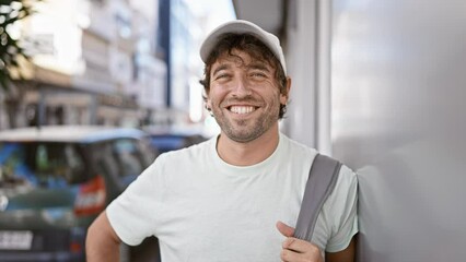 Wall Mural - Smiling man with beard wearing cap and t-shirt standing on city street