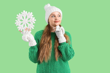 Poster - Beautiful thoughtful young woman in warm clothes with decorative snowflake on green background