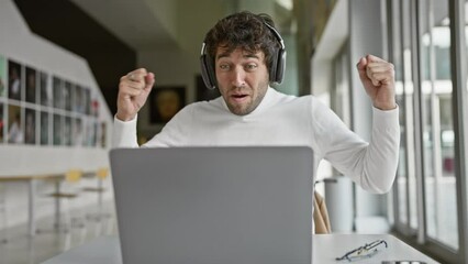 Poster - Hispanic man with headphones at laptop in office reacting with success