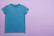 A plain blue t-shirt is laid out on a purple background, with copy space
