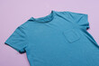 A plain blue t-shirt with a pocket is laid out on a purple background, with copy space
