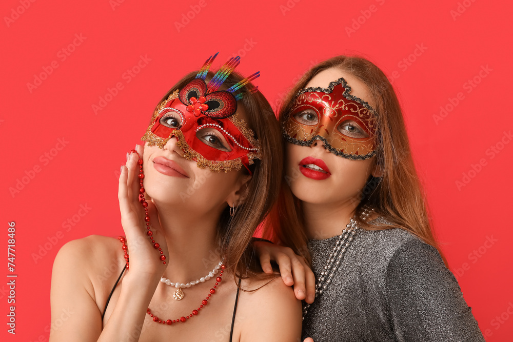 Pretty young women in carnival masks on red background