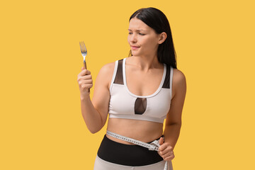 Sticker - Beautiful young displeased woman with fork and measuring tape on yellow background. Weight loss concept