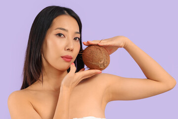 Pretty young Asian woman with coconut on lilac background