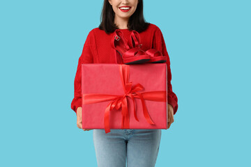 Poster - Beautiful young woman with gift box and stylish high heels on blue background. Valentine's Day celebration