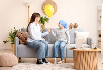 Sticker - Little girl after chemotherapy taking blue balloon from her mother at home. International Childhood Cancer Day