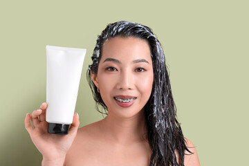 Poster - Young Asian woman with tube of hair mask on green background, closeup