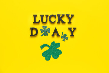 Words LUCKY DAY with clovers for St. Patrick's celebration on yellow background