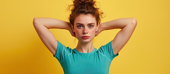 Wall Mural - A young brunette woman with a top knot hairstyle is flexing her arm muscles. She is wearing a teal top and is isolated on a vivid yellow background.