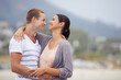 © peopleimages.com - Love, romance and dating for couple at beach for leisure, bonding or vacation. Partners, mates and relationship with smile and hug for kiss and affection against blurred background and mockup
