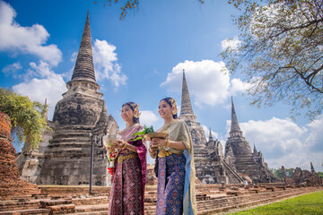 Wall Mural - Asian woman wearing ancient Thai traditional dress holds garland and fresh flowers paying homage Buddha in temple to make a wish on the traditional Songkran festival in Thailand.