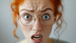 Surprised redhead woman with round glasses.