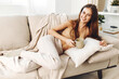 © SHOTPRIME STUDIO - Cozy Morning: Smiling Woman Holding Hot Coffee Mug, Wrapped in Blanket, Relaxing on Sofa in Warm Autumn Room