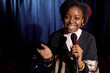 © pressmaster - Happy young female comedian of modern stand up club holding microphone while speaking in front of audience on stage