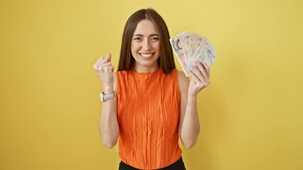 Sticker - Excited hispanic woman clutching england pounds banknotes in joyful victory, proudly raises arm in isolated yellow room, celebrating financial success