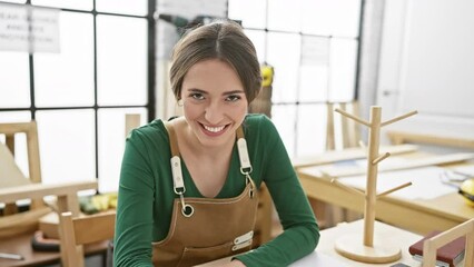 Poster - Stunned hispanic woman carpenter sits with shocked, scared face expression in carpentry workshop, amazed and excited amidst astonishment