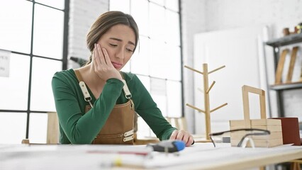 Poster - Clueless hispanic carpenter lady sitting, puzzled expression radiating doubt in carpentry workshop