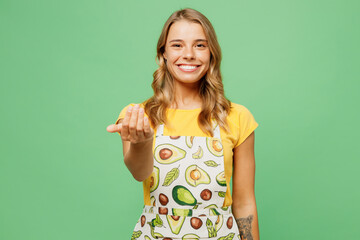 Wall Mural - Young smiling cheerful fun housewife housekeeper chef cook baker woman wear apron yellow t-shirt waving hand pov call follow me isolated on plain pastel green background studio. Cooking food concept.