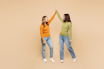 Wall Mural - Full body side view young friends two women they wears orange green shirt casual clothes together meeting together greeting giving high five clapping hands folded isolated on plain beige background.