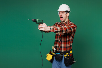 Poster - Young mad employee laborer handyman man wear red shirt hardhat hat use hold electric drill isolated on plain green background Instruments accessories for renovation apartment room Repair home concept