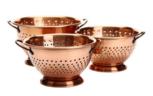 A Set Of Three Metal Colanders Are Neatly Stacked On Top Of Each Other. The Colanders Are Shiny And Show Signs Of Use, With Remnants Of Food Visible On The Edges.